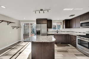 Kitchen featuring light stone countertops, appliances with stainless steel finishes, decorative backsplash, sink, and a kitchen island