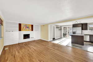 Unfurnished living room with built in shelves, light wood-type flooring, a textured ceiling, and a brick fireplace