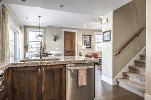 Kitchen with decorative light fixtures, stainless steel dishwasher, dark hardwood / wood-style floors, and sink