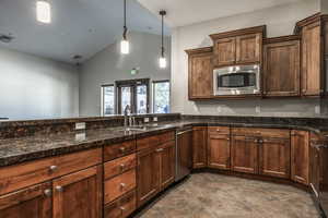 Kitchen featuring lofted ceiling, dark stone counters, sink, decorative light fixtures, and stainless steel appliances