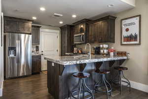 Kitchen featuring a breakfast bar, dark wood-type flooring, kitchen peninsula, dark brown cabinets, and appliances with stainless steel finishes