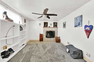 Carpeted living room featuring a tile fireplace, ceiling fan, and a textured ceiling