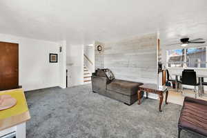 Living room featuring carpet flooring, ceiling fan, a textured ceiling, and wooden walls