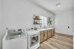 Laundry area with separate washer and dryer, sink, cabinets, and light wood-type flooring