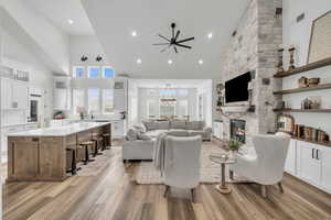 Living room featuring sink, light hardwood / wood-style flooring, ceiling fan, a towering ceiling, and a fireplace