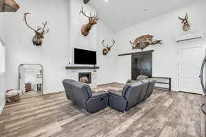 Living room with beamed ceiling, a stone fireplace, an AC wall unit, and hardwood / wood-style floors