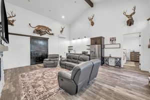 Living room with beamed ceiling, a wall mounted air conditioner, light hardwood / wood-style floors, and high vaulted ceiling