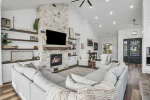 Living room with a fireplace, dark hardwood / wood-style floors, high vaulted ceiling, and ceiling fan