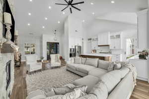 Living room featuring ceiling fan, wood-type flooring, a fireplace, and high vaulted ceiling