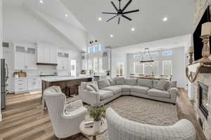 Living room featuring ceiling fan, light hardwood / wood-style floors, a fireplace, and high vaulted ceiling