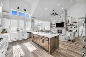 Kitchen featuring a stone fireplace, white cabinets, high vaulted ceiling, a kitchen island, and appliances with stainless steel finishes