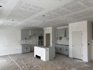 Kitchen featuring wall chimney range hood, a center island, and gray cabinetry