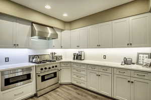 Kitchen featuring high end stove, light hardwood / wood-style floors, white cabinetry, and wall chimney range hood