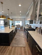 Kitchen featuring gas range, a textured ceiling, a spacious island, sink, and decorative light fixtures