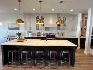 Kitchen featuring light stone countertops, a spacious island, custom range hood, and a breakfast bar area