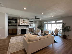 Living room with a fireplace, dark hardwood / wood-style flooring, a textured ceiling, and ceiling fan