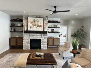 Living room featuring hardwood / wood-style floors, a textured ceiling, a stone fireplace, and ceiling fan