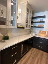 Bar with light stone countertops, light hardwood / wood-style floors, white cabinetry, and beverage cooler