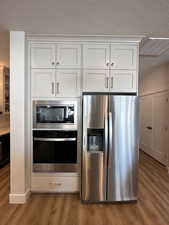 Kitchen with a textured ceiling, stainless steel appliances, white cabinetry, and light hardwood / wood-style flooring