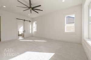 Unfurnished bedroom with connected bathroom, a barn door, ceiling fan, and light colored carpet