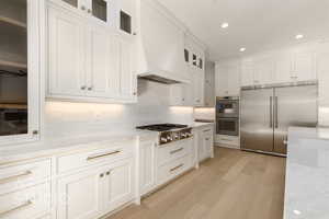 Kitchen with white cabinets, ceiling fan, light stone countertops, appliances with stainless steel finishes, and custom range hood