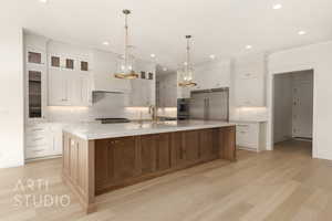 Kitchen with a large island, white cabinets, light wood-type flooring, and appliances with stainless steel finishes