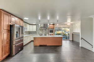 Kitchen with a kitchen island with sink, wall chimney exhaust hood, decorative backsplash, decorative light fixtures, and stainless steel appliances