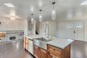 Kitchen featuring pendant lighting, a center island with sink, sink, stainless steel dishwasher, and ornamental molding