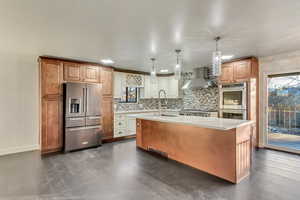 Kitchen with sink, wall chimney range hood, pendant lighting, a kitchen island with sink, and appliances with stainless steel finishes