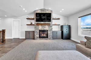 Living room with vaulted ceiling, hardwood / wood-style flooring, and a stone fireplace