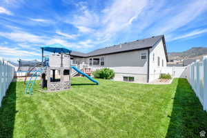 Back of property with a playground, a mountain view, a trampoline, and a lawn