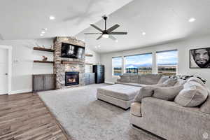 Living room featuring lofted ceiling, a stone fireplace, light hardwood / wood-style flooring, ceiling fan, and a textured ceiling