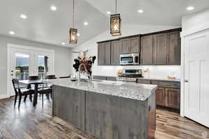 Kitchen featuring light stone countertops, pendant lighting, stainless steel appliances, and dark brown cabinets