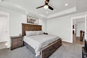 Carpeted bedroom featuring a tray ceiling and ceiling fan