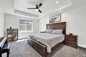 Bedroom featuring carpet flooring, a raised ceiling, and ceiling fan