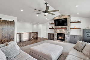 Living room featuring ceiling fan, a stone fireplace, lofted ceiling, and carpet floors