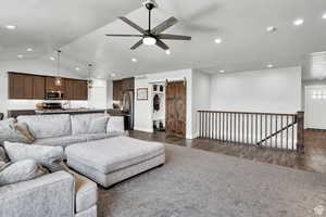 Living room featuring dark hardwood / wood-style flooring, a barn door, ceiling fan, and lofted ceiling