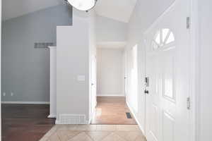 Entrance foyer with high vaulted ceiling, light wood-style floors, and baseboards