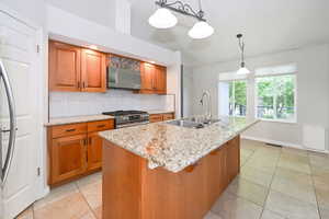 Kitchen featuring a sink, range hood, appliances with stainless steel finishes, tasteful backsplash, and brown cabinets