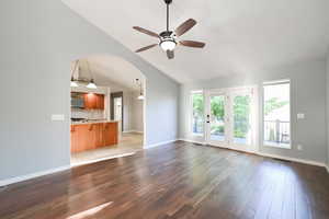 Unfurnished living room with a ceiling fan, light wood finished floors, baseboards, arched walkways, and high vaulted ceiling