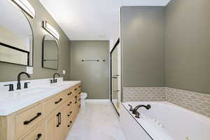 Full bathroom featuring a garden tub, marble finish floors, double vanity, a shower stall, and toilet