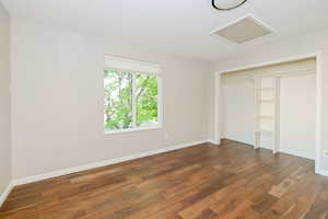Unfurnished bedroom featuring wood finished floors, attic access, a closet, and baseboards
