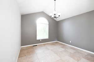 Empty room with a chandelier, lofted ceiling, light tile patterned flooring, and baseboards