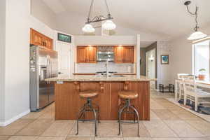 Kitchen featuring pendant lighting, backsplash, vaulted ceiling, light stone countertops, and stainless steel appliances