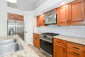 Kitchen featuring appliances with stainless steel finishes, a sink, tasteful backsplash, and brown cabinetry