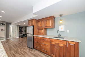 Kitchen featuring light stone countertops, light wood-type flooring, sink, decorative light fixtures, and stainless steel refrigerator