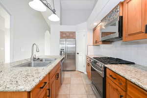 Kitchen featuring appliances with stainless steel finishes, a sink, tasteful backsplash, pendant lighting, and light stone counters