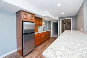 Kitchen featuring freestanding refrigerator, a sink, brown cabinetry, wood finished floors, and light stone countertops