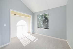 Carpeted spare room featuring vaulted ceiling and baseboards