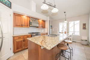 Kitchen with appliances with stainless steel finishes, vaulted ceiling, sink, a center island with sink, and hanging light fixtures